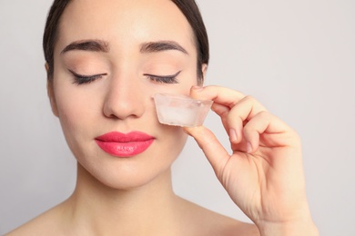 Photo of Young woman with ice cube on light background. Skin care