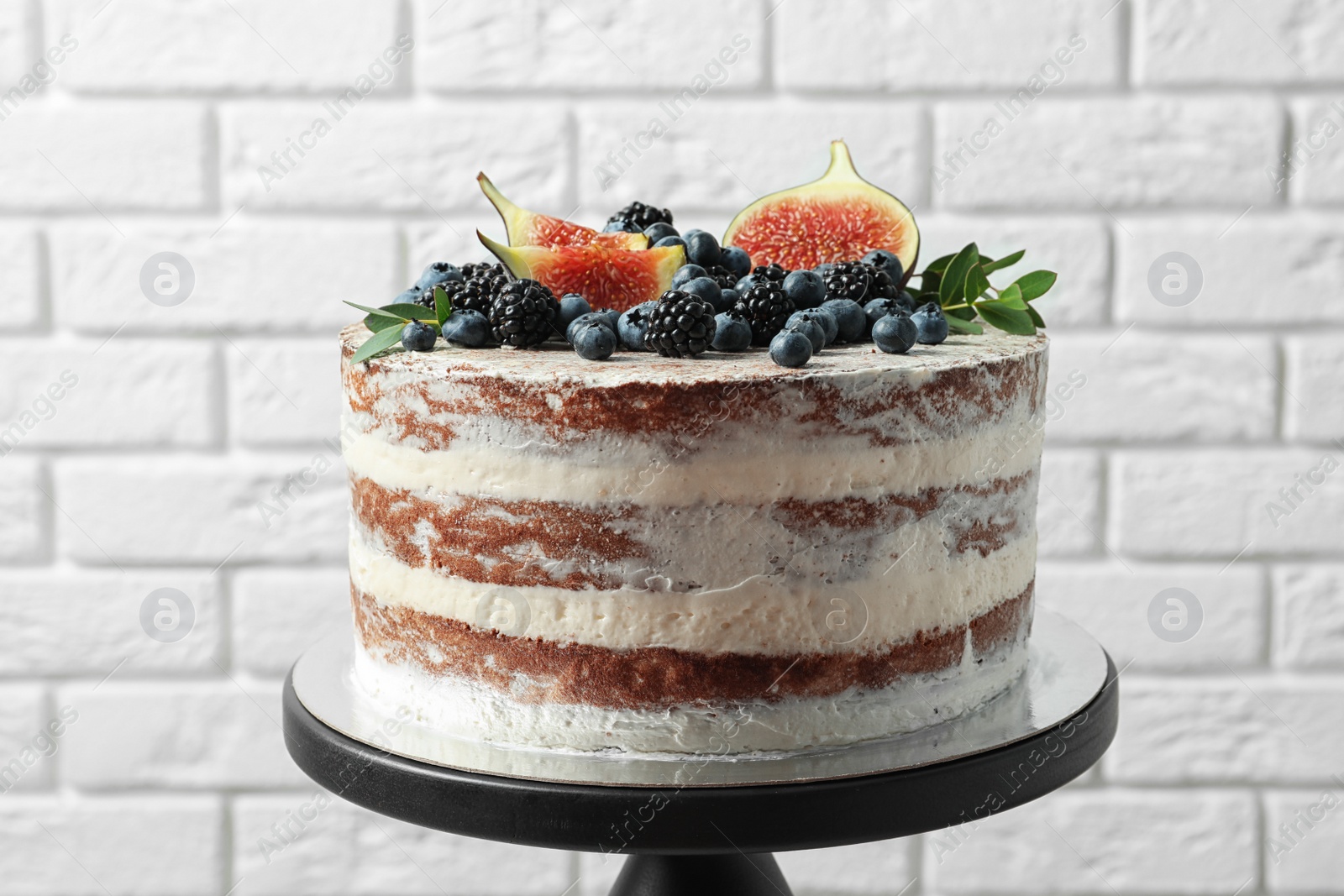 Photo of Delicious homemade cake with fresh berries on stand near brick wall