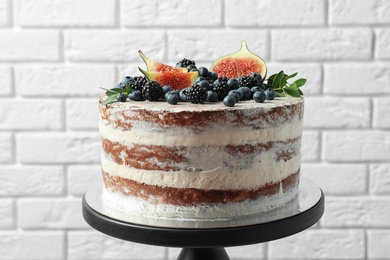 Delicious homemade cake with fresh berries on stand near brick wall