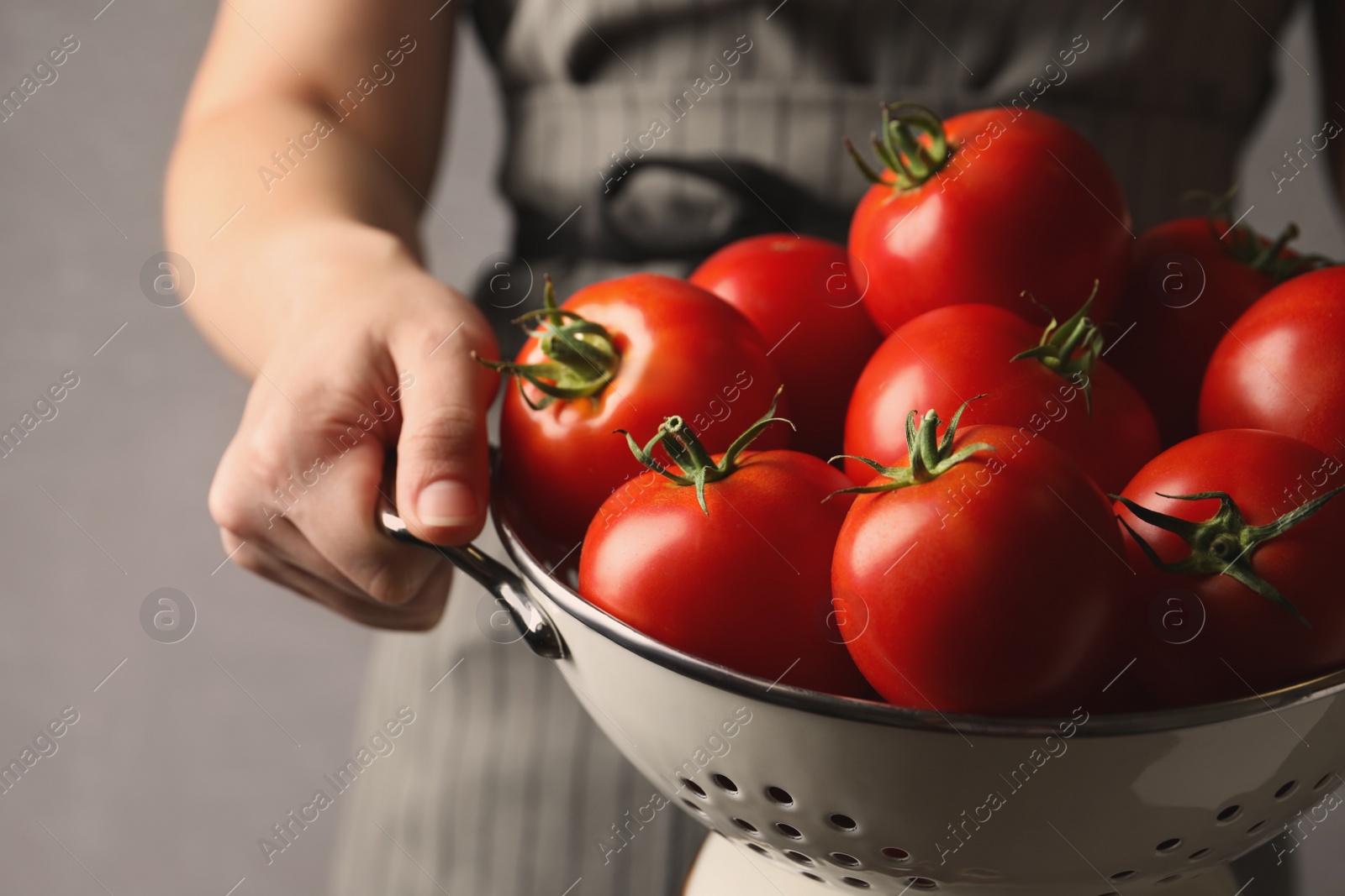 Photo of Woman with colander of ripe tomatoes on grey background, closeup