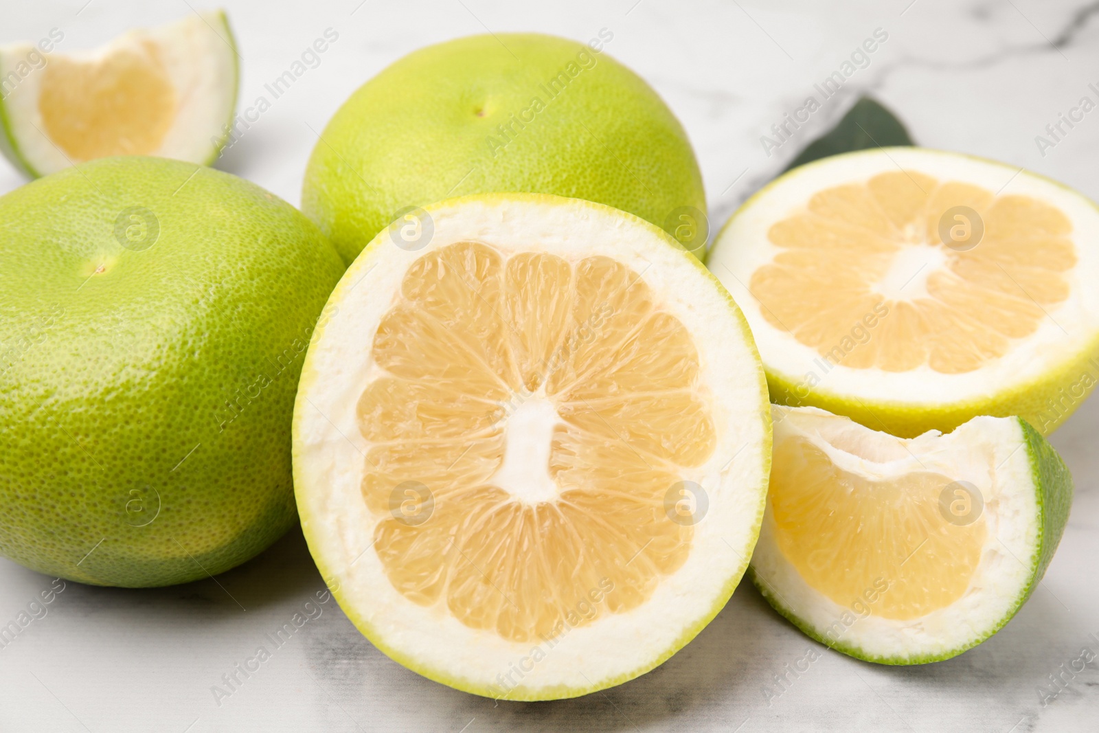 Photo of Whole and cut sweetie fruits on white marble table, closeup