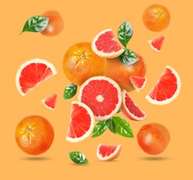 Tasty ripe grapefruits and green leaves falling on orange background