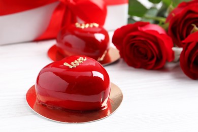 St. Valentine's Day. Delicious heart shaped cakes, roses and gift on white wooden table, closeup