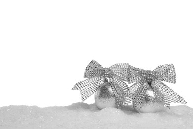 Beautiful silver Christmas balls with bows on snow against white background