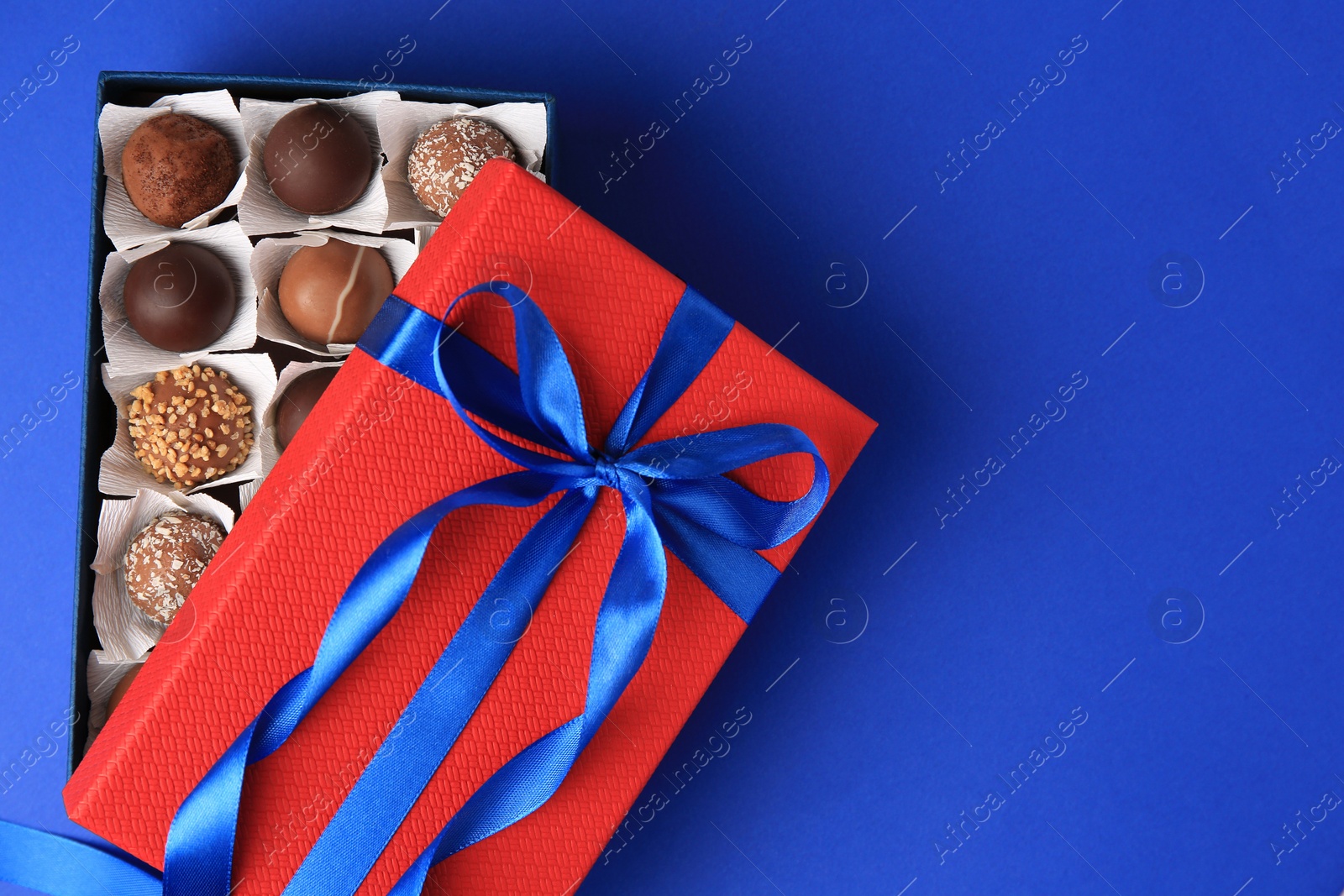 Photo of Box with delicious chocolate candies on blue background, top view. Space for text