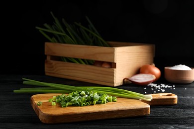 Photo of Chopped green spring onion and stems on black wooden table