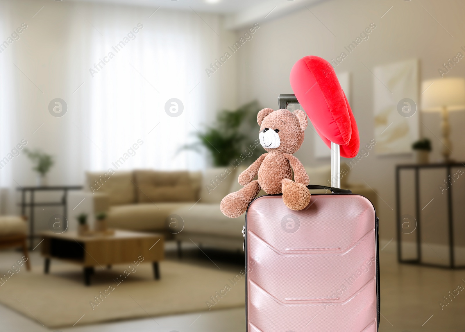 Image of Travel pillow and teddy bear on suitcase in room. Space for text