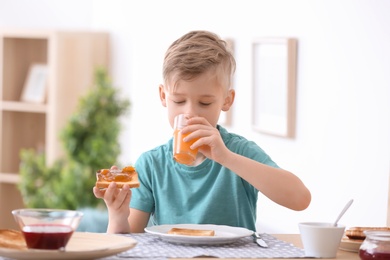 Cute little boy eating tasty toasted bread with jam at table