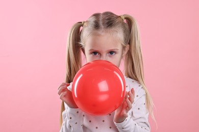 Photo of Cute little girl inflating red balloon on pink background