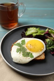 Photo of Plate with tasty fried egg, slice of bread and salad on light blue wooden table, closeup