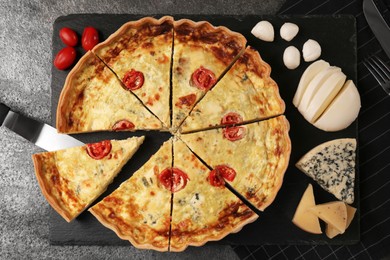 Photo of Taking piece of delicious homemade cheese quiche and ingredients on gray table, flat lay