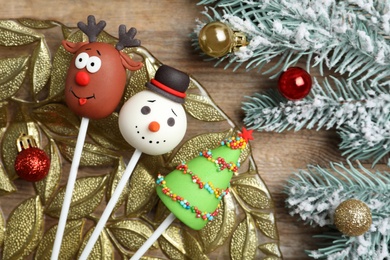 Photo of Delicious Christmas themed cake pops and fir tree branches with balls on wooden table, flat lay