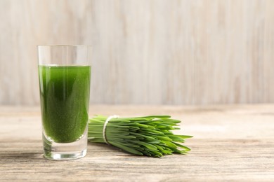 Photo of Wheat grass drink in shot glass and fresh green sprouts on wooden table, closeup. Space for text