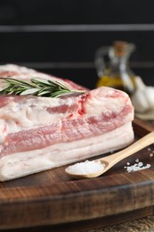 Photo of Piece of raw pork belly, salt and rosemary on wooden table, closeup