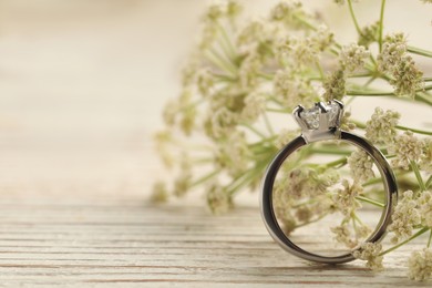 Beautiful engagement ring with gemstone and flowers on white wooden table, closeup. Space for text