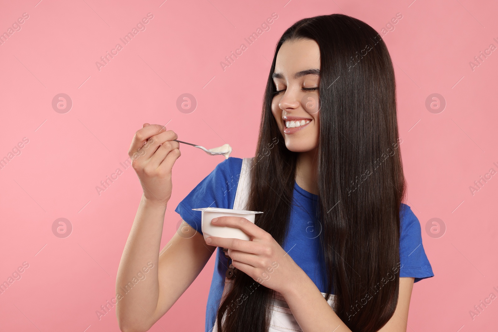 Photo of Happy teenage girl with delicious yogurt and spoon on pink background