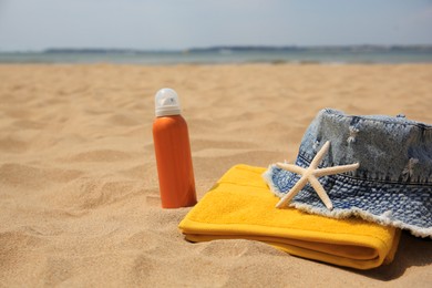 Sunscreen, panama hat, starfish and towel on sandy beach, space for text. Sun protection