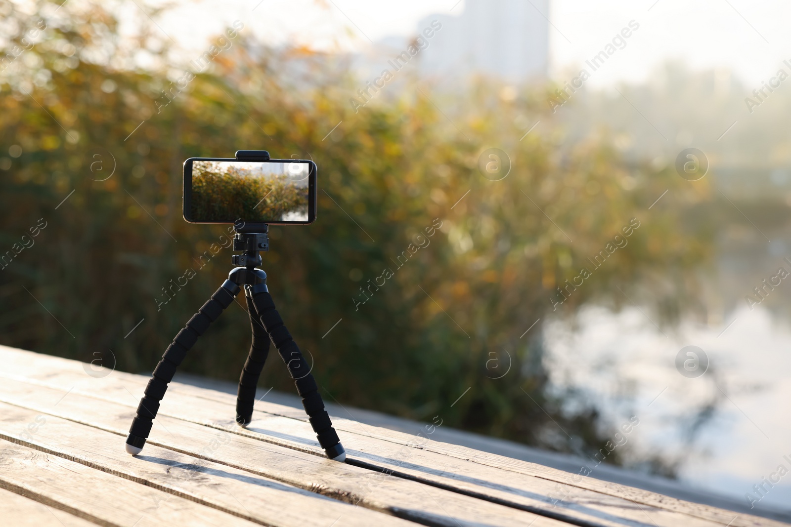 Photo of Tripod with smartphone on wooden pier near river