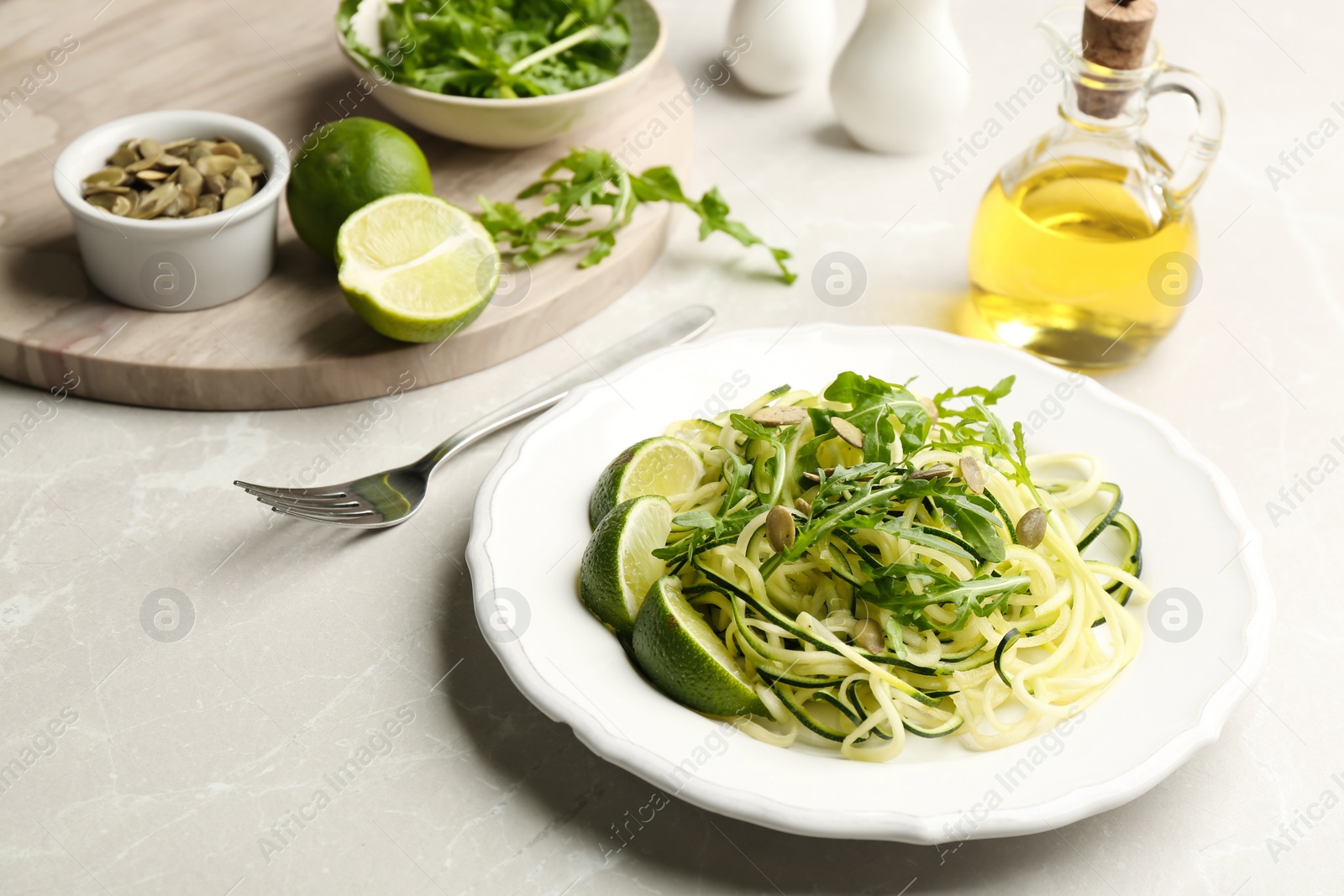 Photo of Delicious zucchini pasta with lime, pumpkin seeds and arugula served on light grey table
