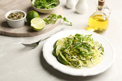 Photo of Delicious zucchini pasta with lime, pumpkin seeds and arugula served on light grey table