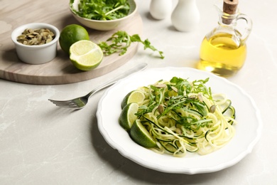 Delicious zucchini pasta with lime, pumpkin seeds and arugula served on light grey table