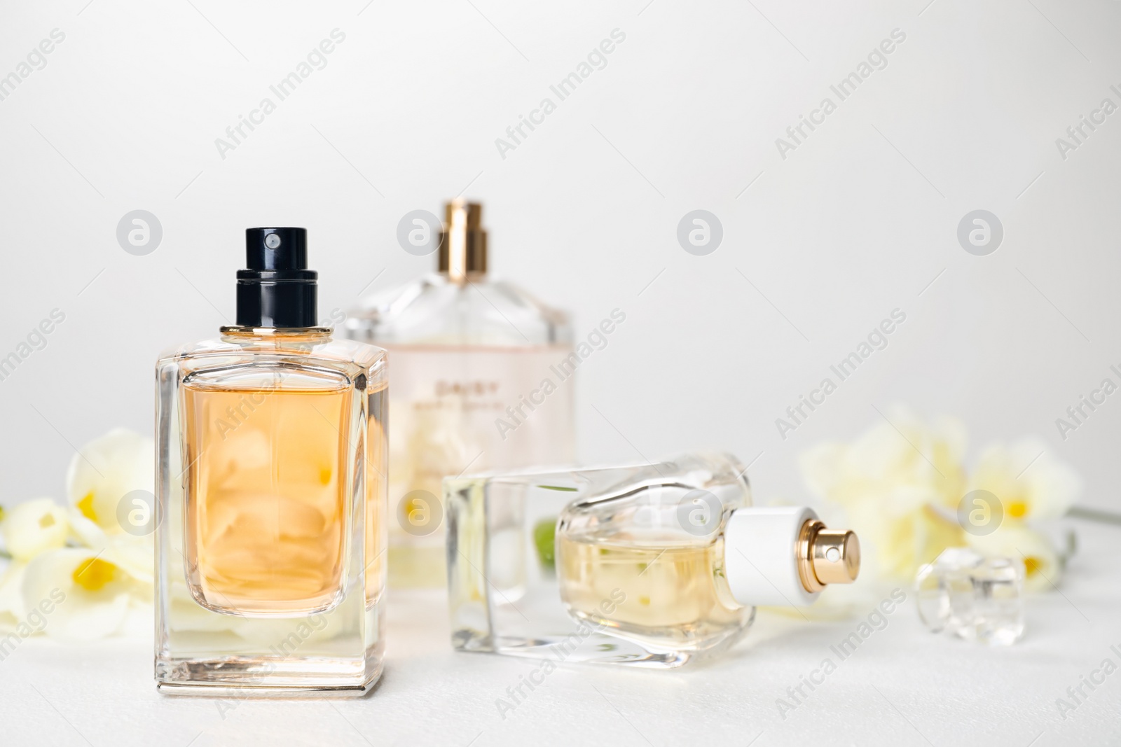 Photo of Perfume bottles and flowers on table against light background