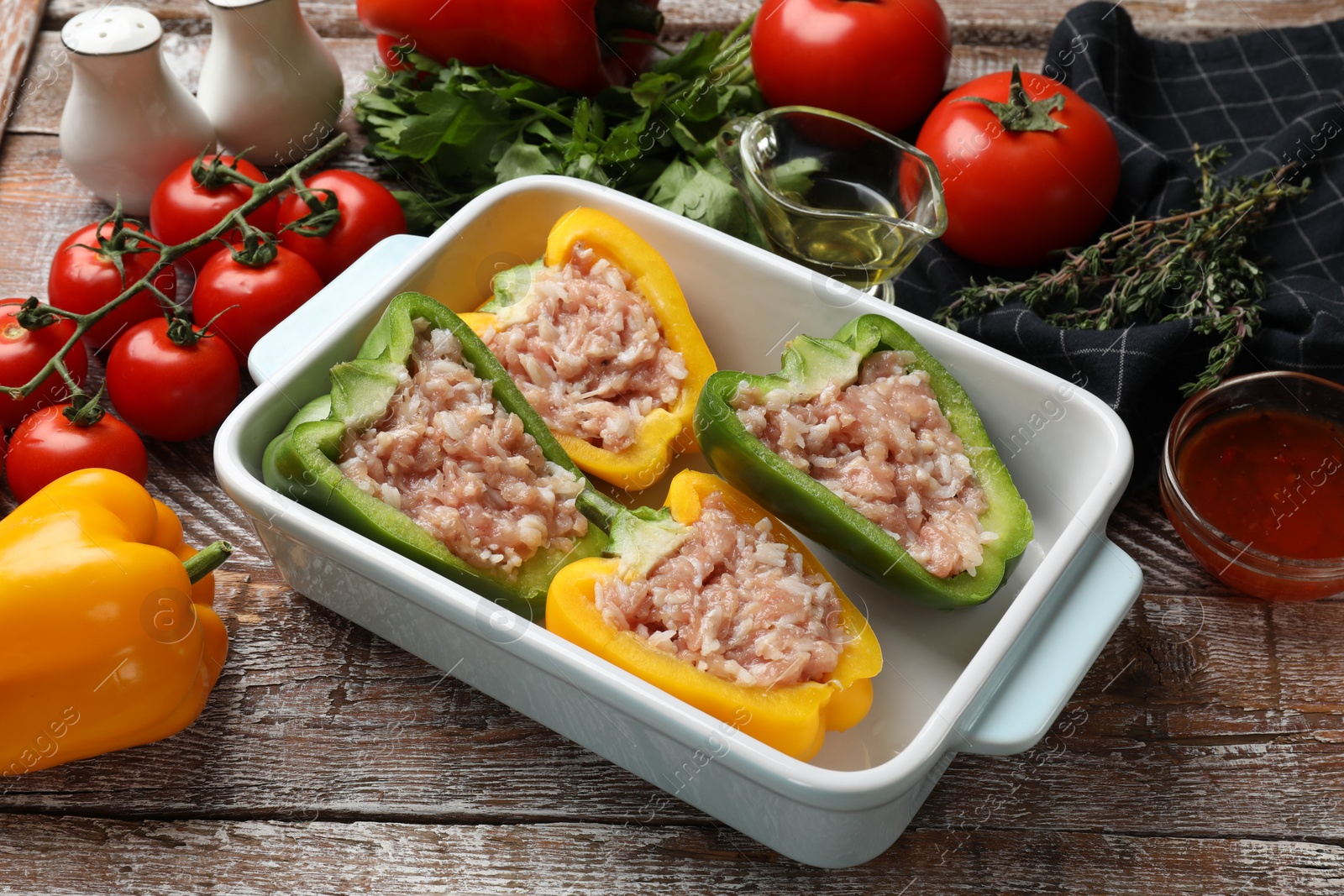 Photo of Raw stuffed peppers in dish and ingredients on wooden table