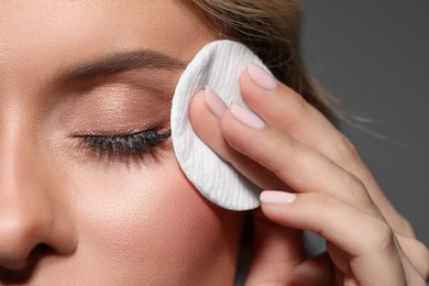 Photo of Beautiful woman removing makeup with cotton pad on dark grey background, closeup