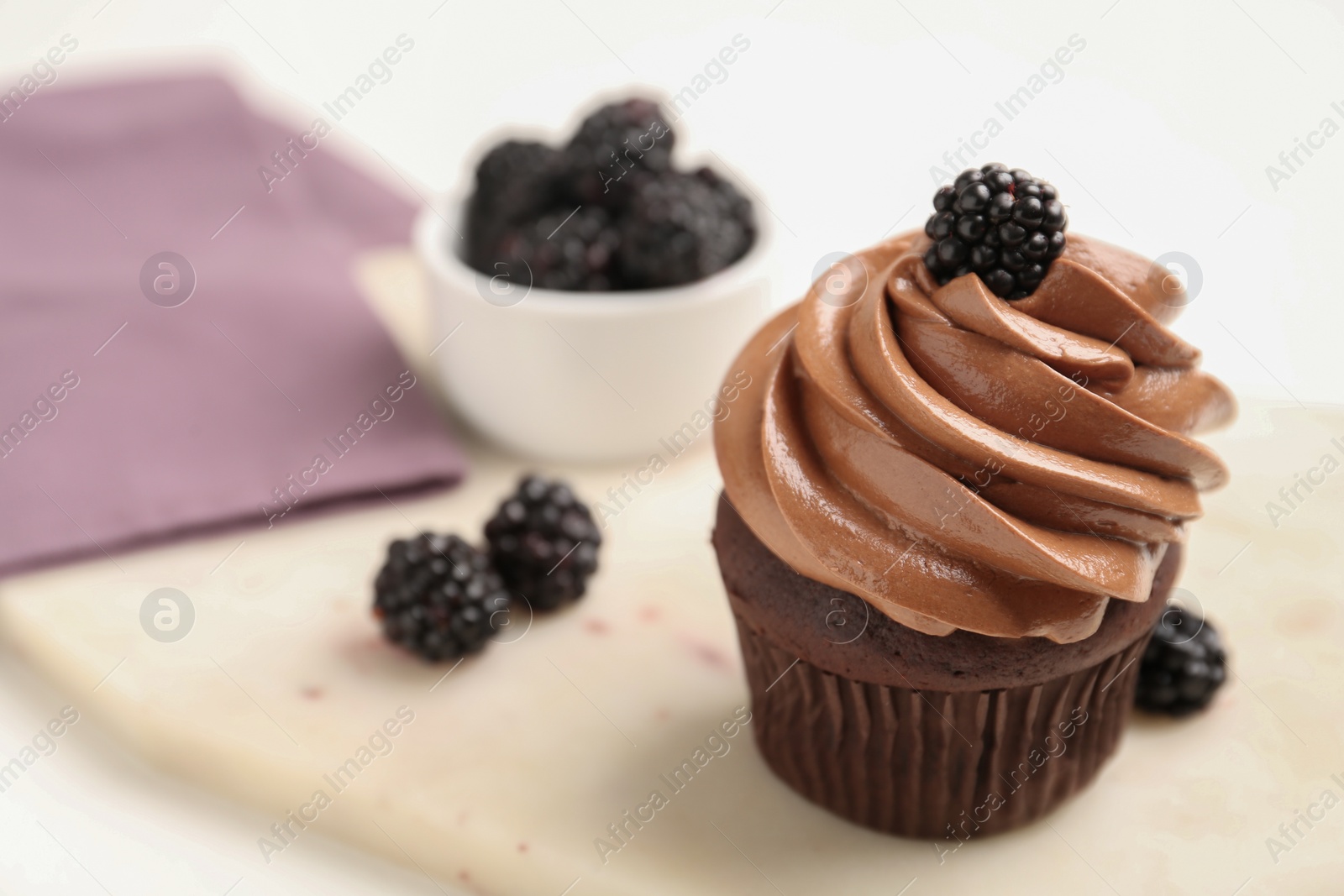 Photo of Delicious chocolate cupcake with cream and blackberries on white board, closeup. Space for text