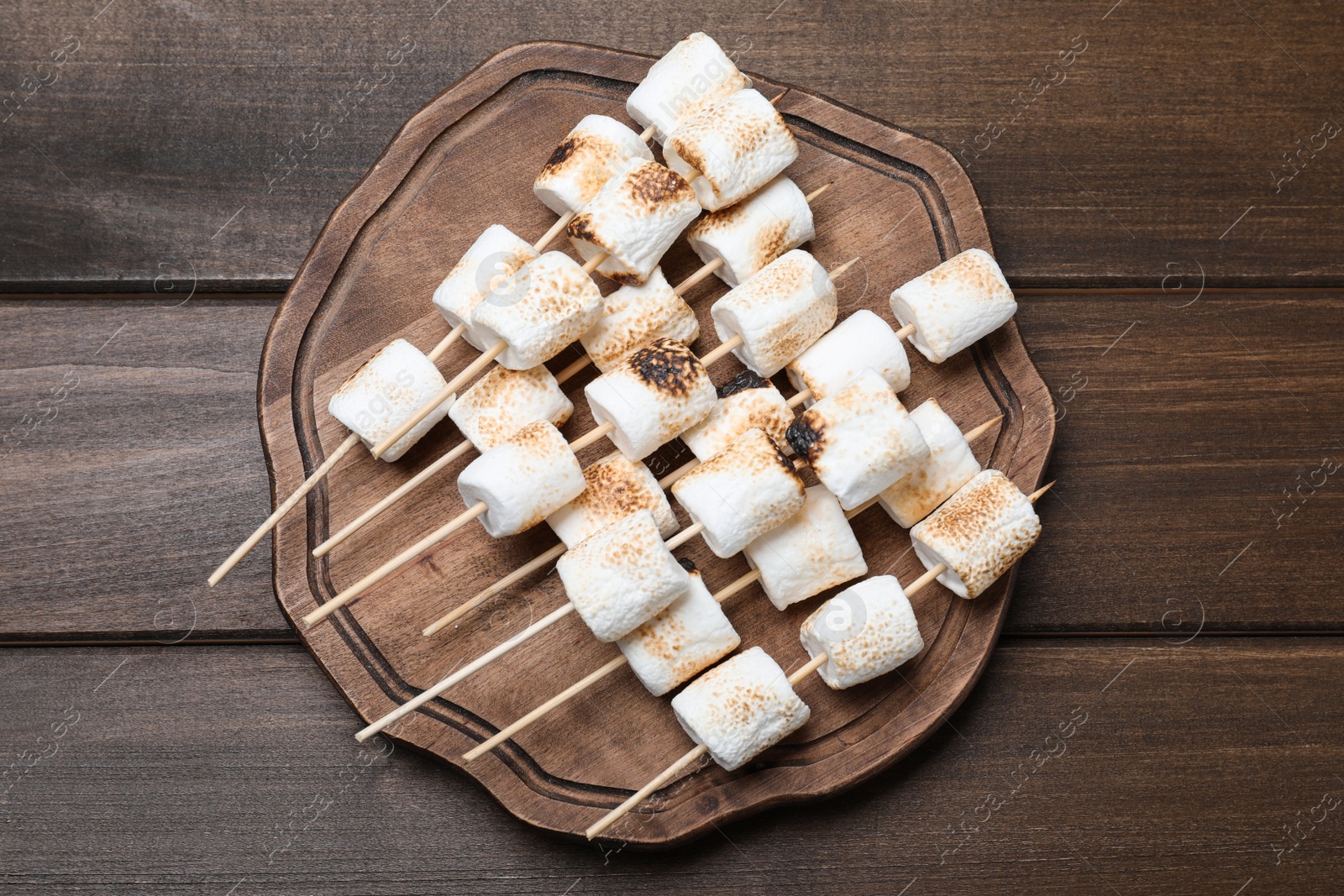 Photo of Sticks with roasted marshmallows on wooden table, top view