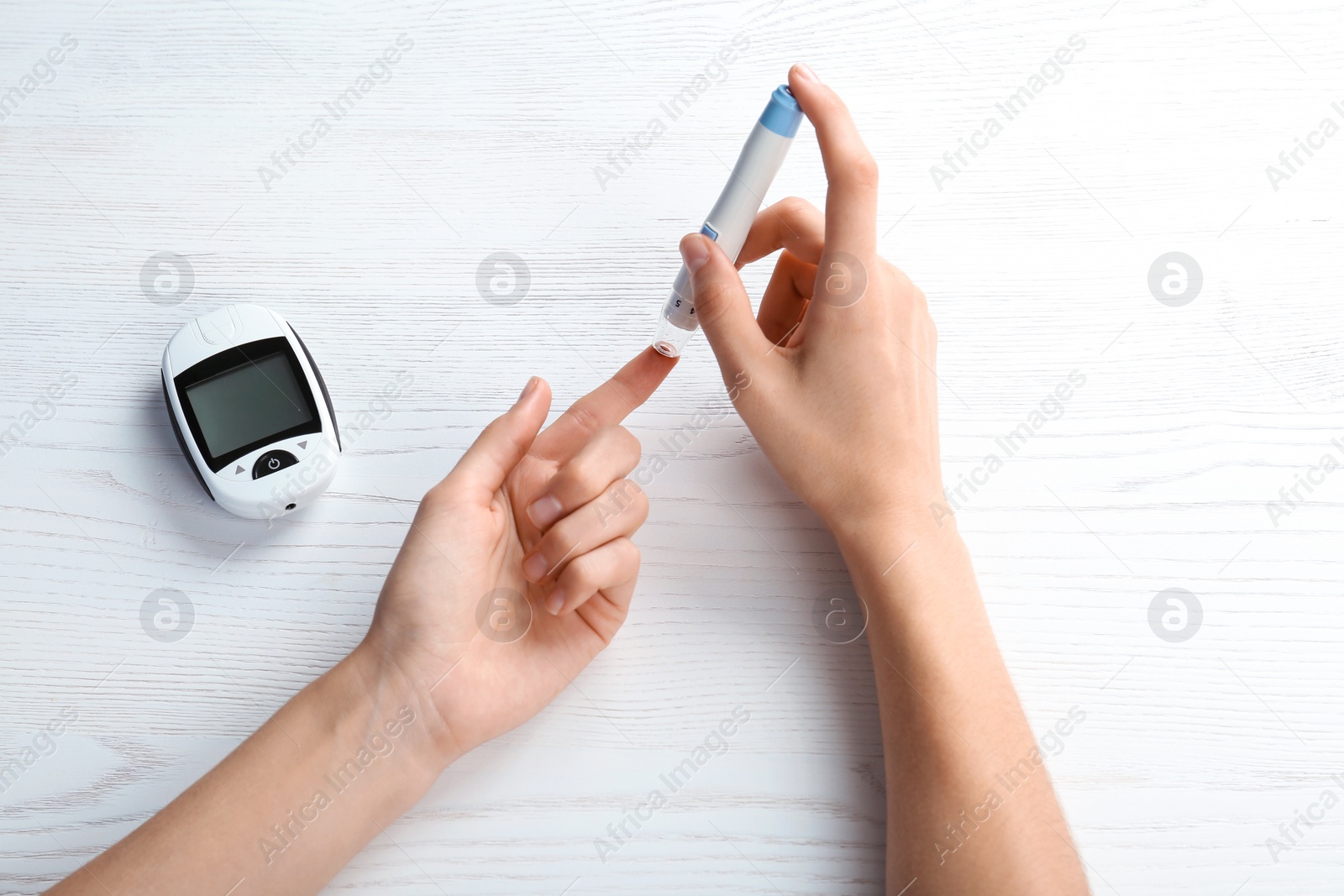 Photo of Woman using lancet pen at table. Diabetes test