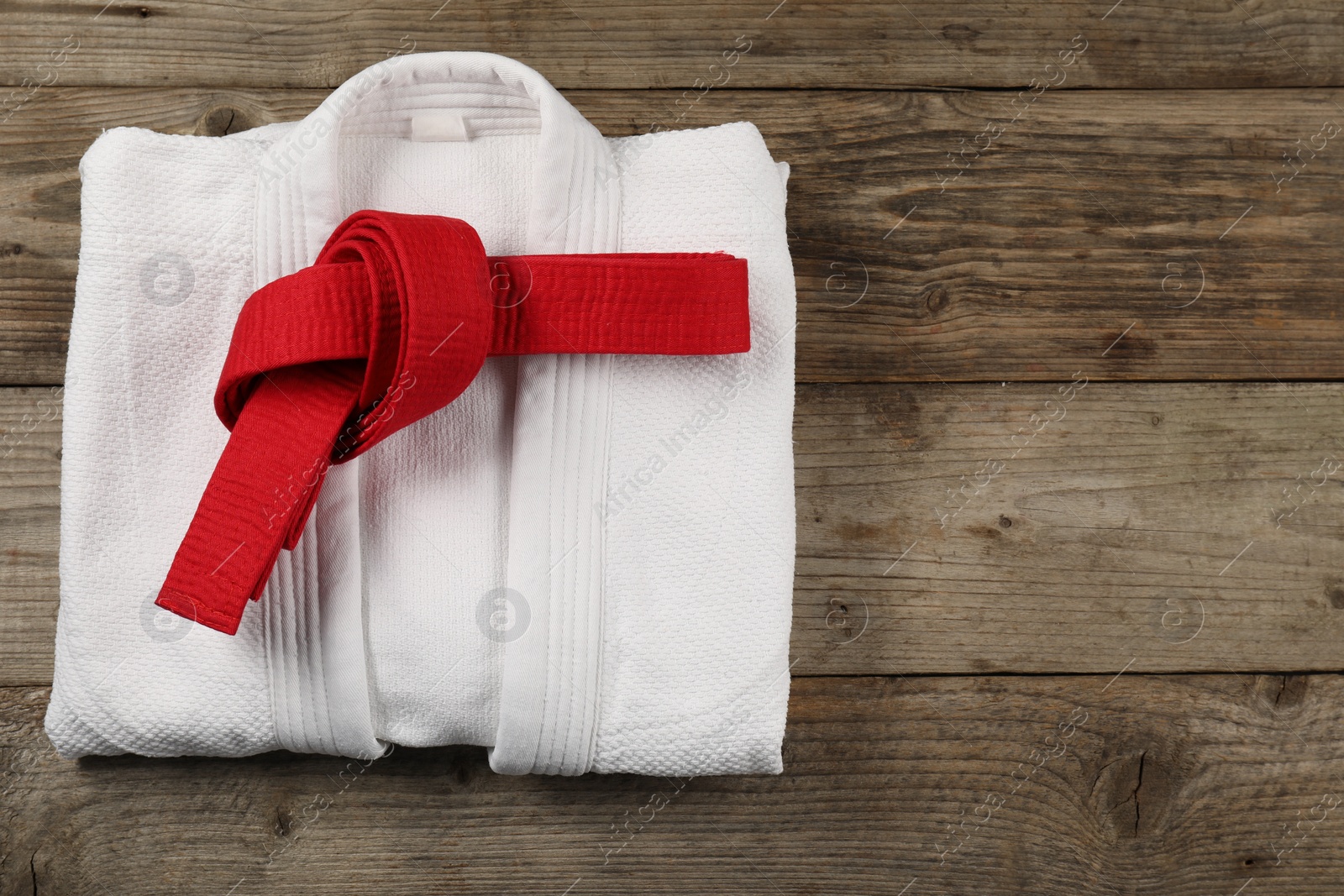 Photo of Red karate belt and white kimono on wooden background, top view. Space for text