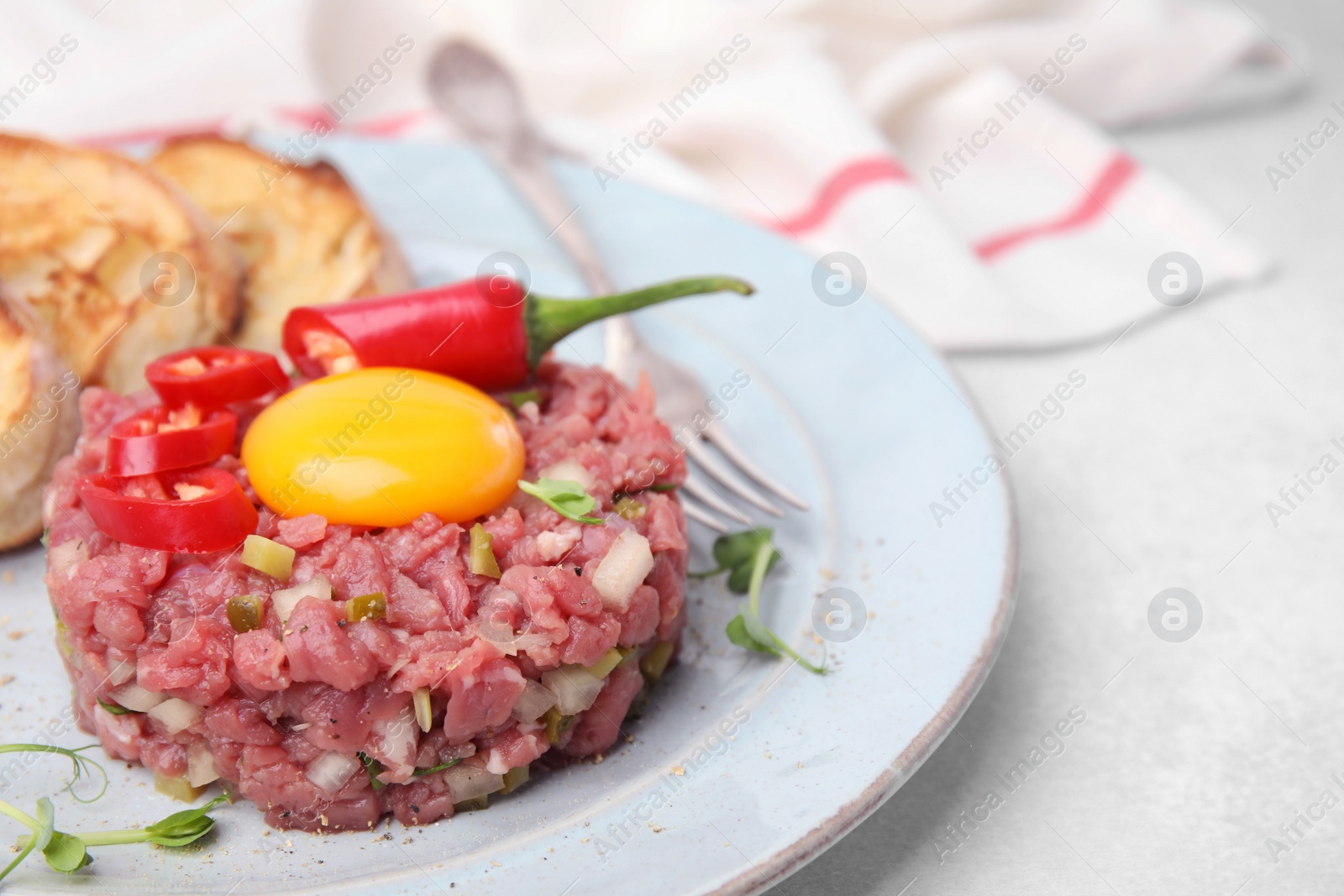 Photo of Tasty beef steak tartare served with yolk and other accompaniments on white table, closeup. Space for text