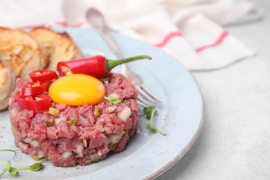 Tasty beef steak tartare served with yolk and other accompaniments on white table, closeup. Space for text