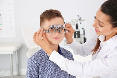 Children's doctor putting trial frame on little boy in clinic. Eye examination