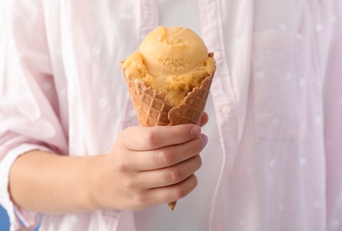 Woman holding yellow ice cream in wafer cone, closeup