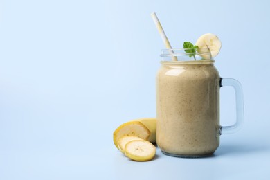 Photo of Mason jar with delicious fruit smoothie and fresh banana on light blue background. Space for text