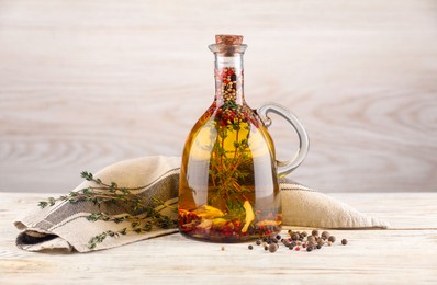 Photo of Glass jug of cooking oil with spices and herbs on white wooden table