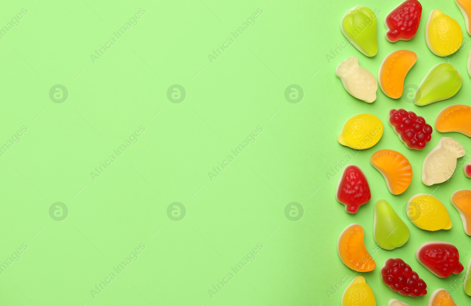 Photo of Delicious gummy fruit shaped candies on green background, flat lay. Space for text