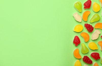 Delicious gummy fruit shaped candies on green background, flat lay. Space for text