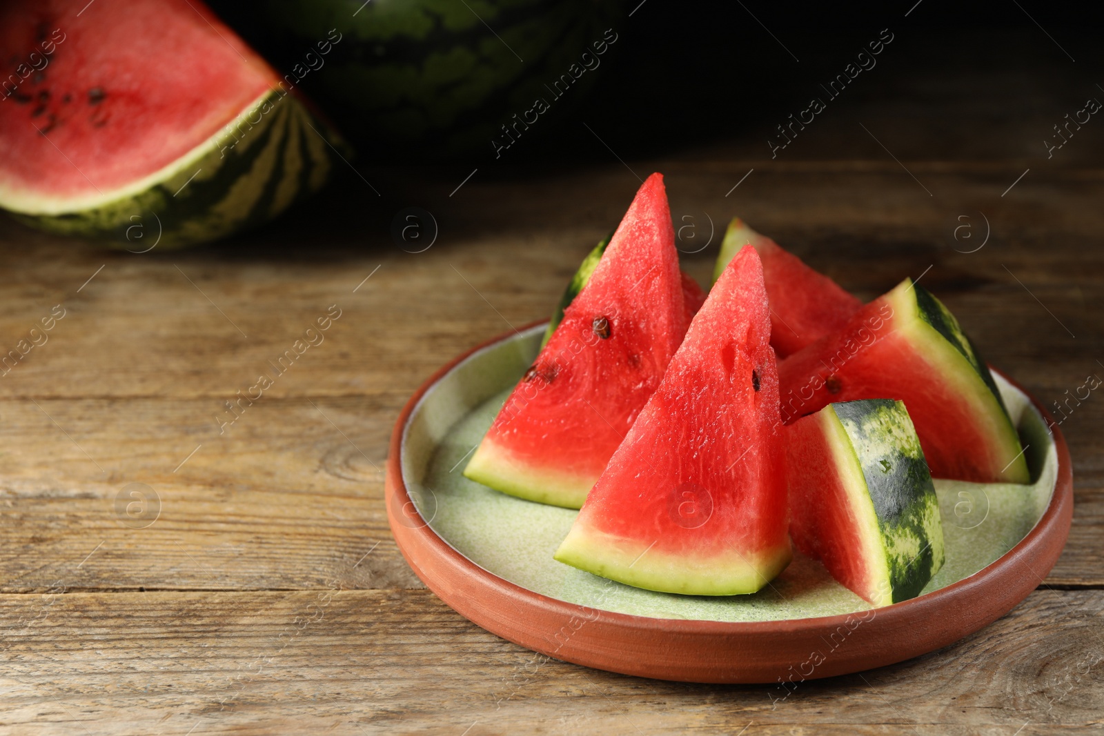 Photo of Plate with slices of juicy watermelon on wooden table, space for text