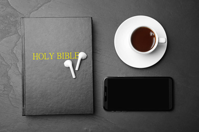 Bible, phone, cup of coffee and earphones on black background, flat lay. Religious audiobook