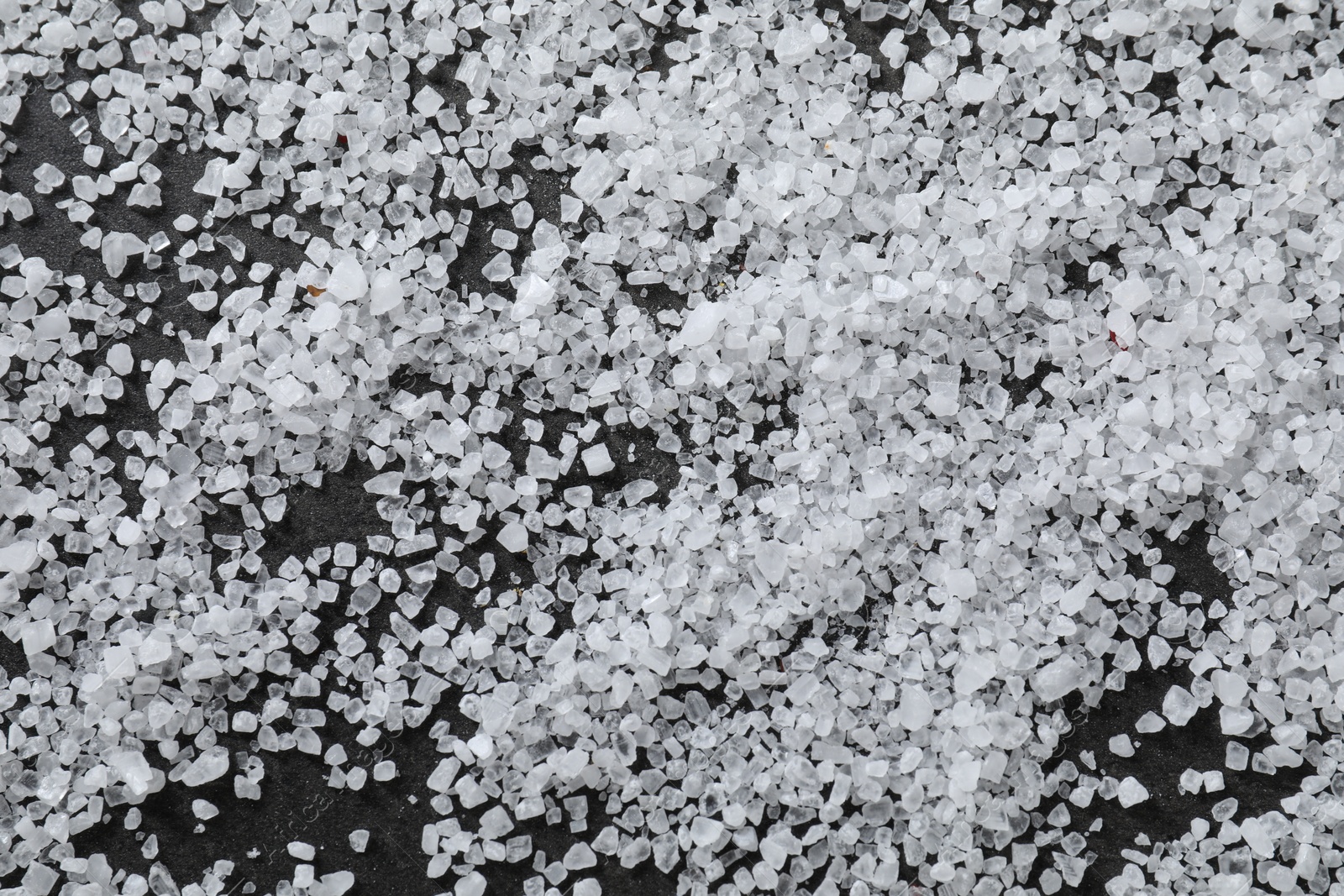 Photo of Scattered white natural salt on black table, top view