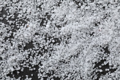 Photo of Scattered white natural salt on black table, top view