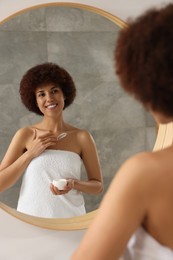 Photo of Beautiful young woman applying cream onto body in bathroom