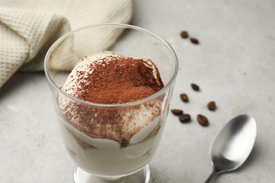 Photo of Delicious tiramisu in glass, spoon and scattered coffee beans on light table, closeup