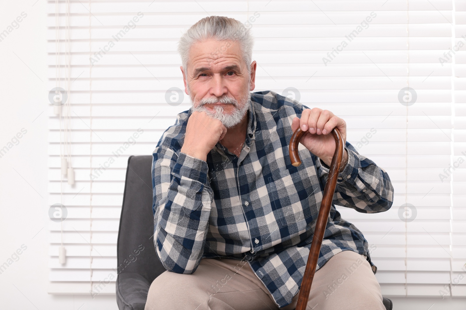 Photo of Senior man with walking cane sitting on armchair at home