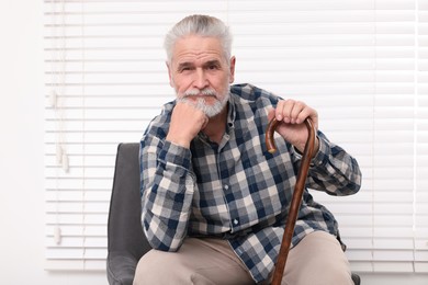 Senior man with walking cane sitting on armchair at home