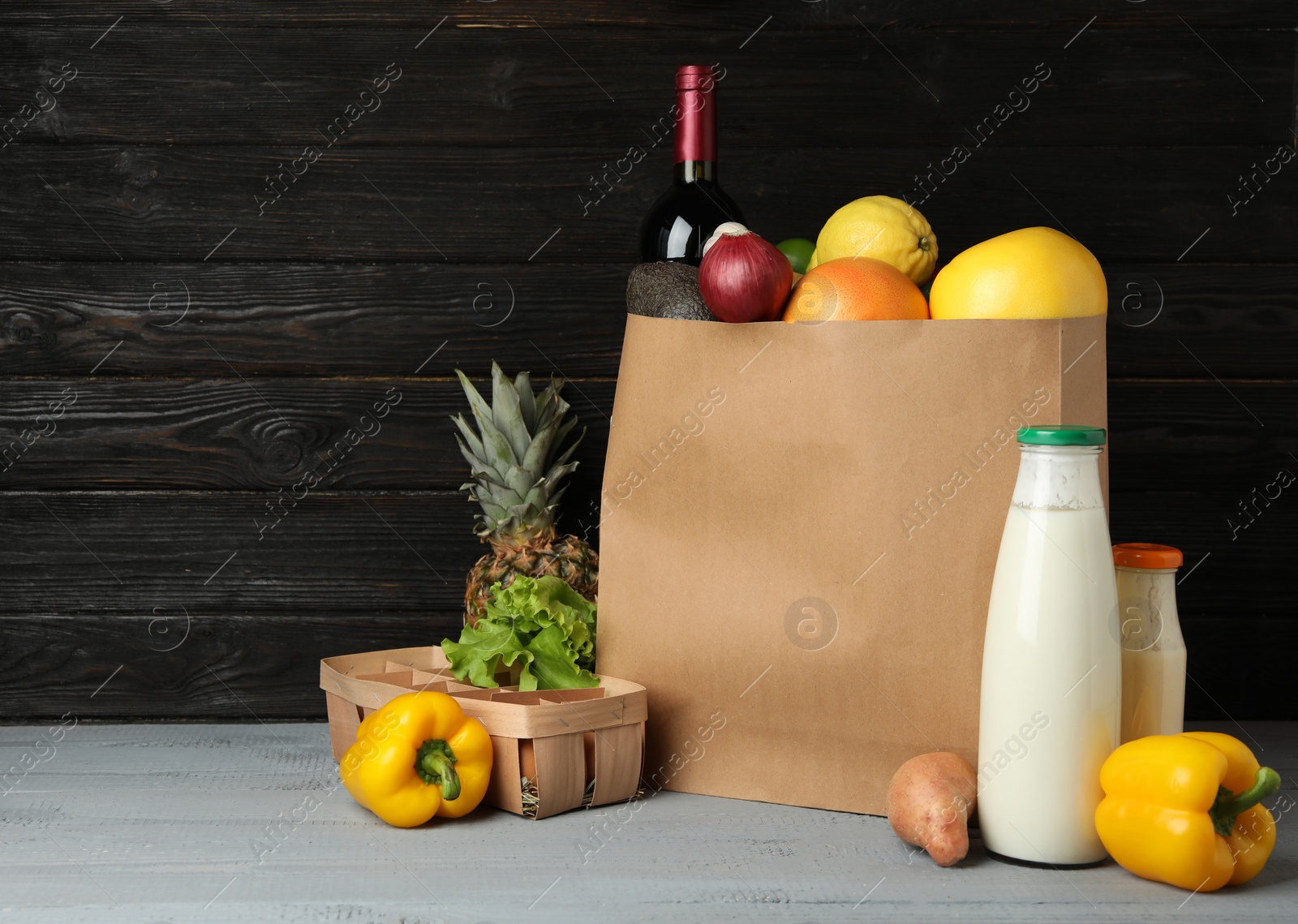 Photo of Paper bag with groceries on wooden table against dark background. Space for text