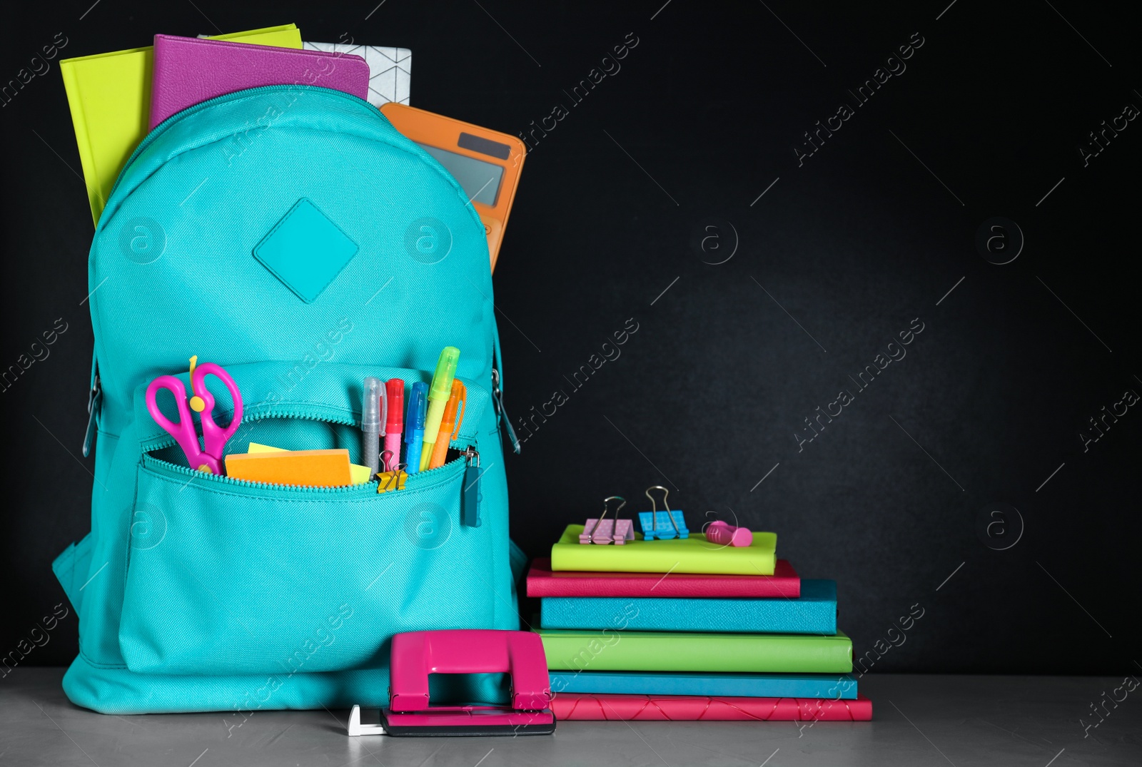 Photo of Bright backpack with school stationery on grey stone table against black background